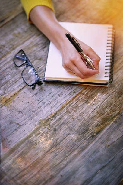 Cropped shot of a woman sitting at a table and writing in her notepad outside